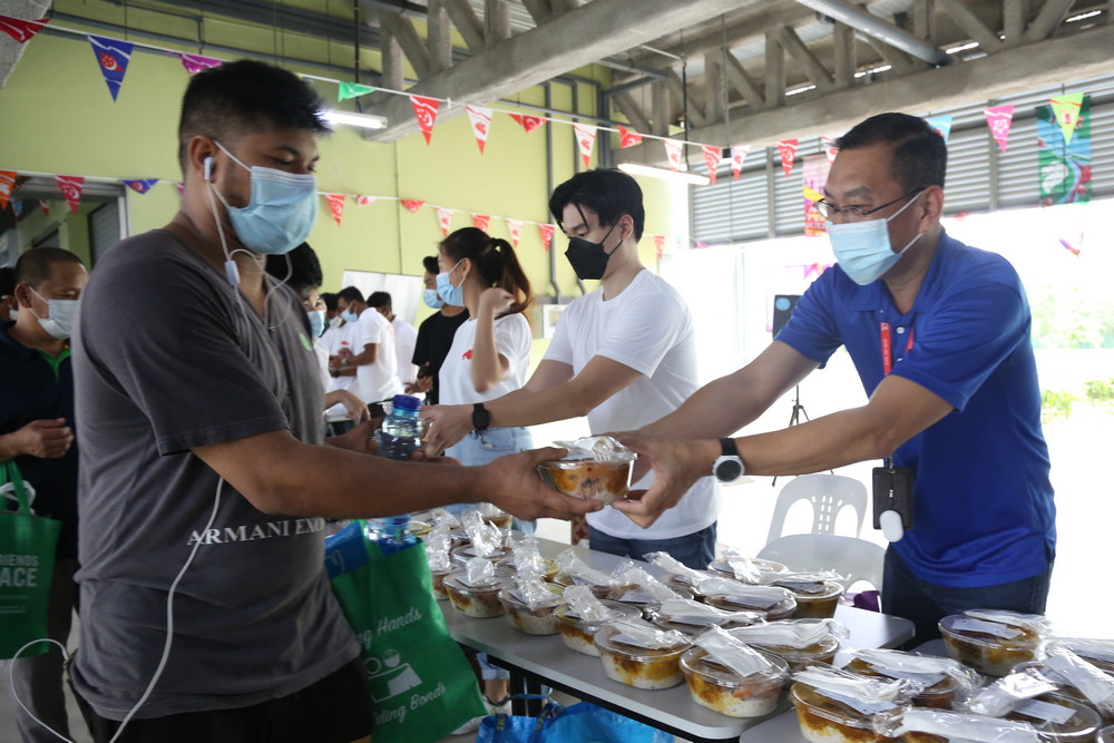 Mr Poh Lye Hin (in blue), MOM Regional Commander (Central) and Guest of Honour, helping to serve lunch packed in Tzu Chi eco-friendly lunchboxes. These lunchboxes were given free, courtesy of generous Tzu Chi donors, with notes attached encouraging the workers to reuse them. (Photo by Alice Toh)